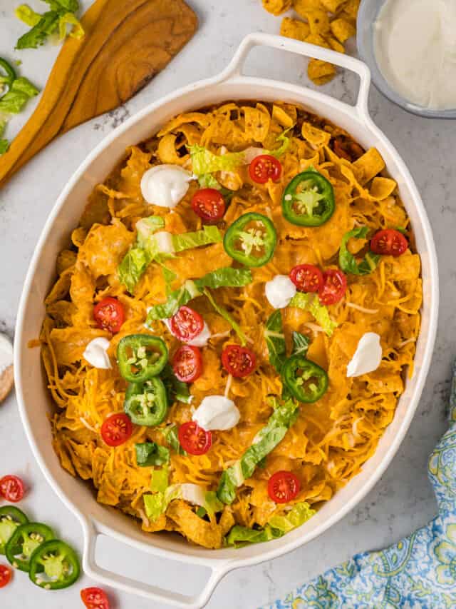 Walking taco casserole topped with dollops of sour cream and jalapeno slices.