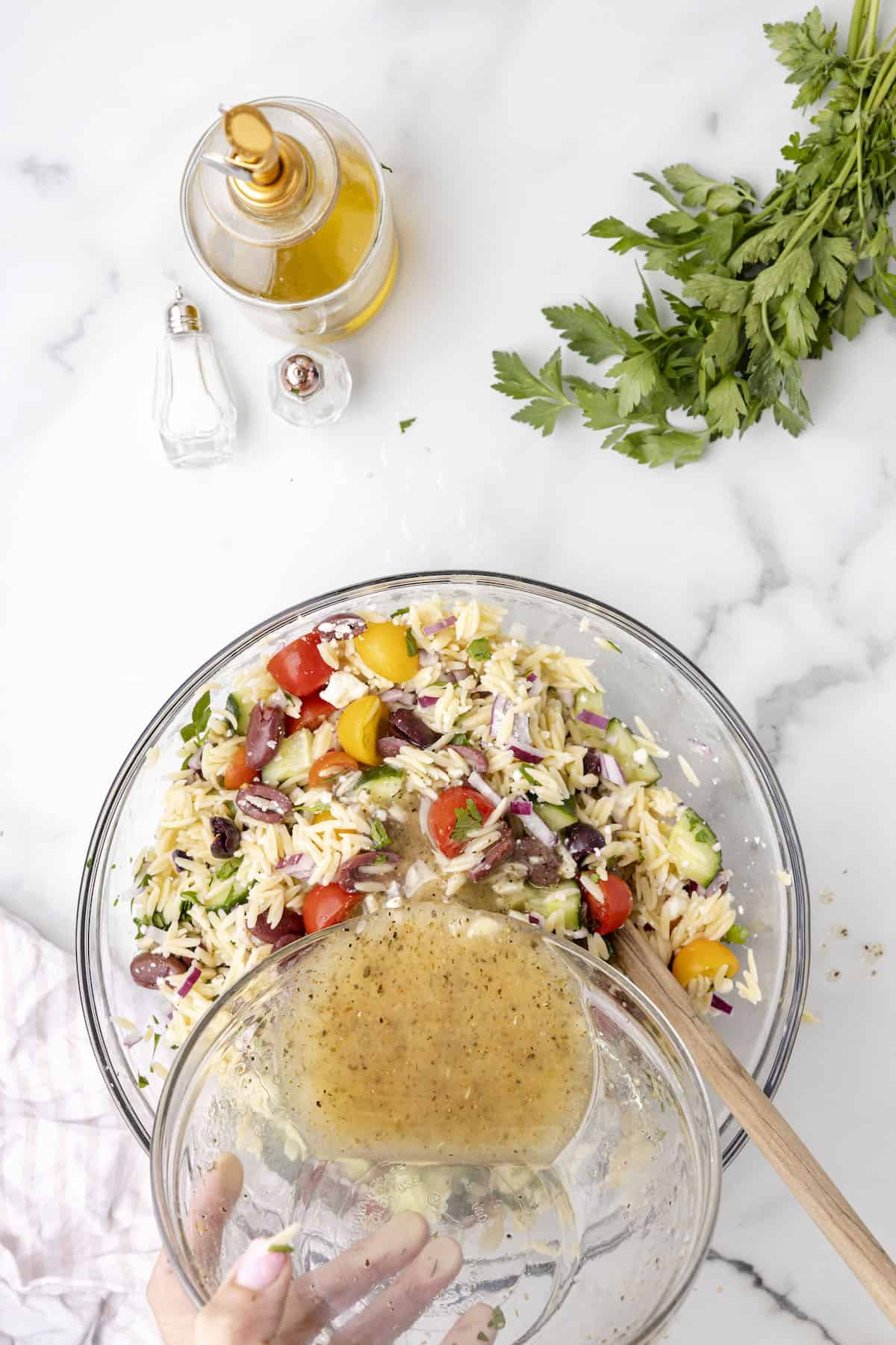 Making a orzo salad in a large glass bowl with olive oil and herbs.