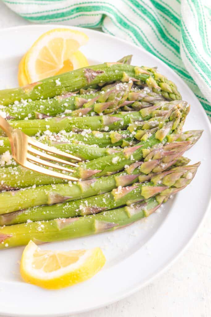 A fork in tender asparagus cooked in the instant pot with lemon wedges on the side.