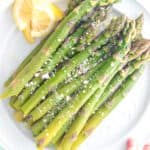 Cooked asparagus on a plate with lemon and a sprinkling of parmesan cheese