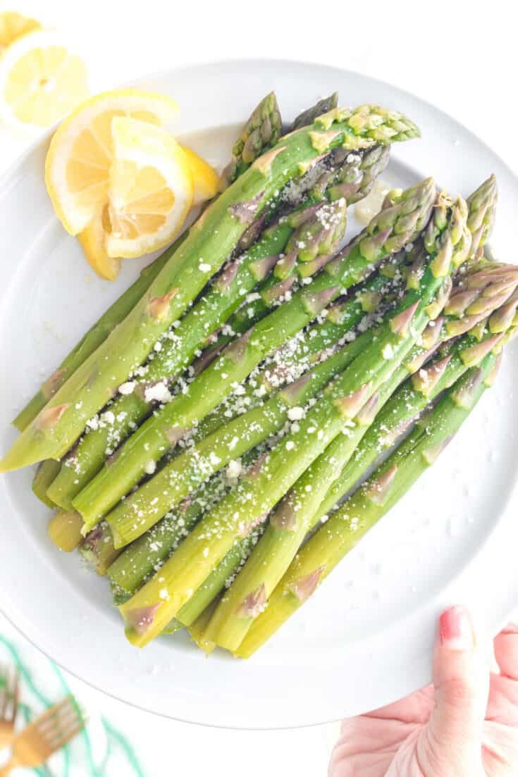 Cooked asparagus on a plate with lemon and a sprinkling of parmesan cheese
