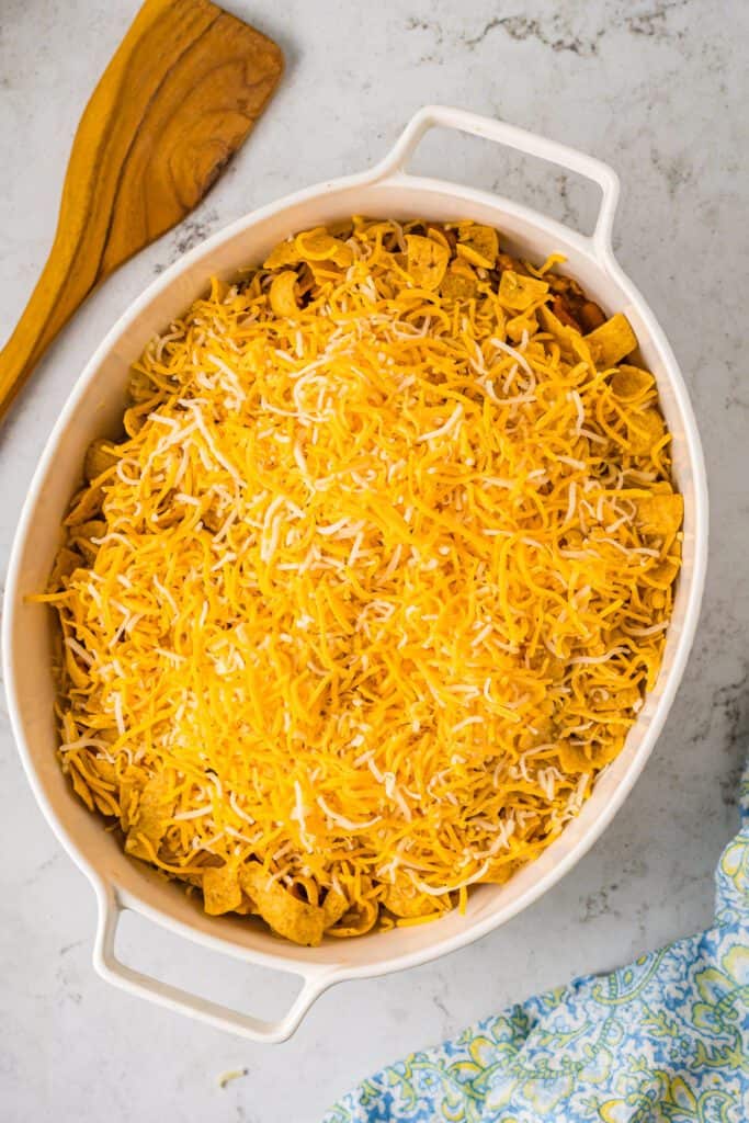 White casserole dish topped with frito chips and shredded cheese.