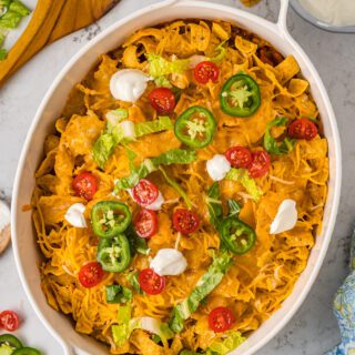 Walking taco casserole topped with dollops of sour cream and jalapeno slices.