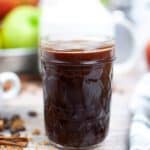 A jar of apple cider syrup on a wood countertop.