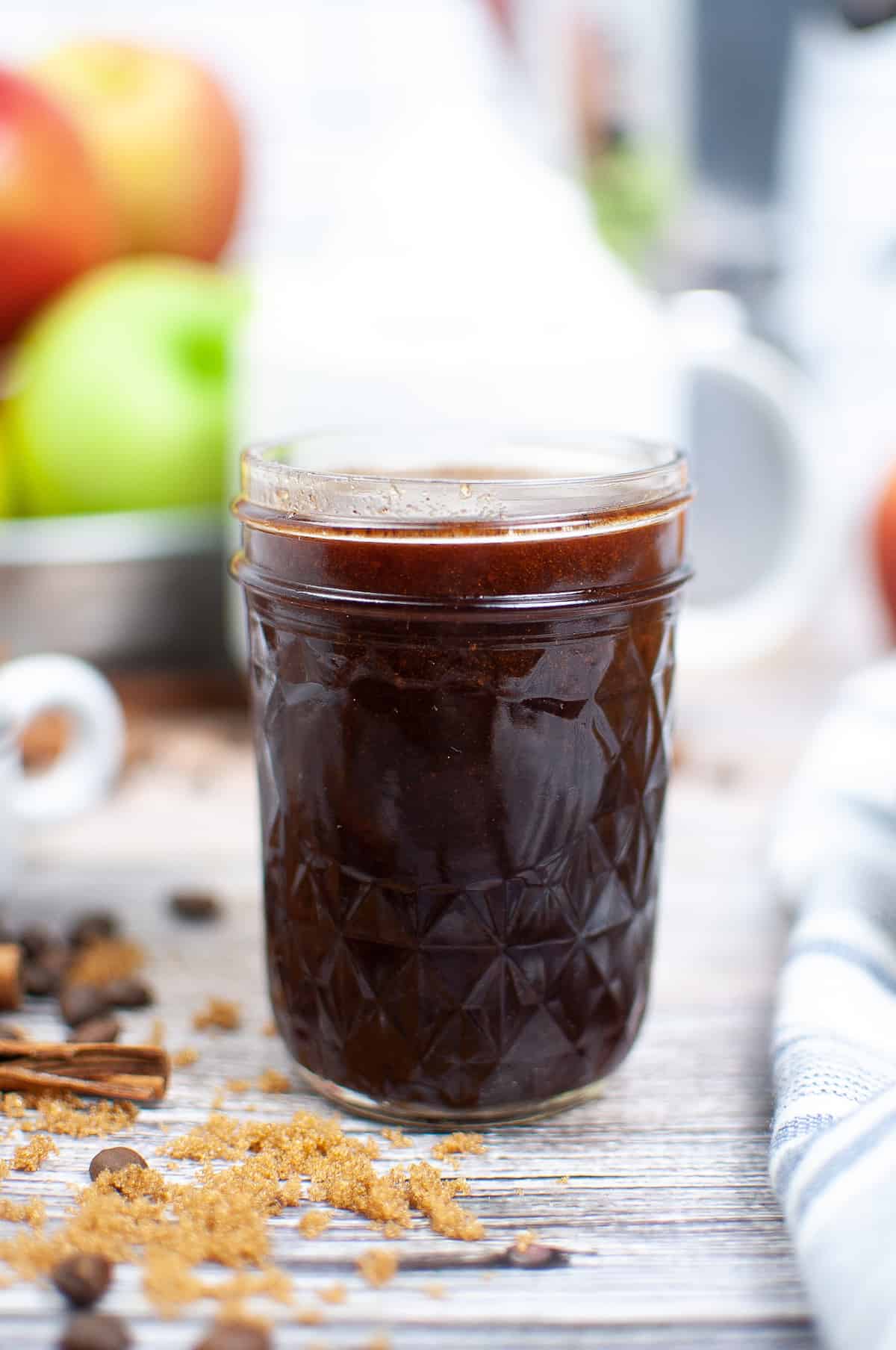 A jar of apple cider syrup on a wood countertop.