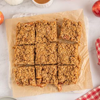 Cut apple crumble bars on a wooden cutting board with apples on the side.