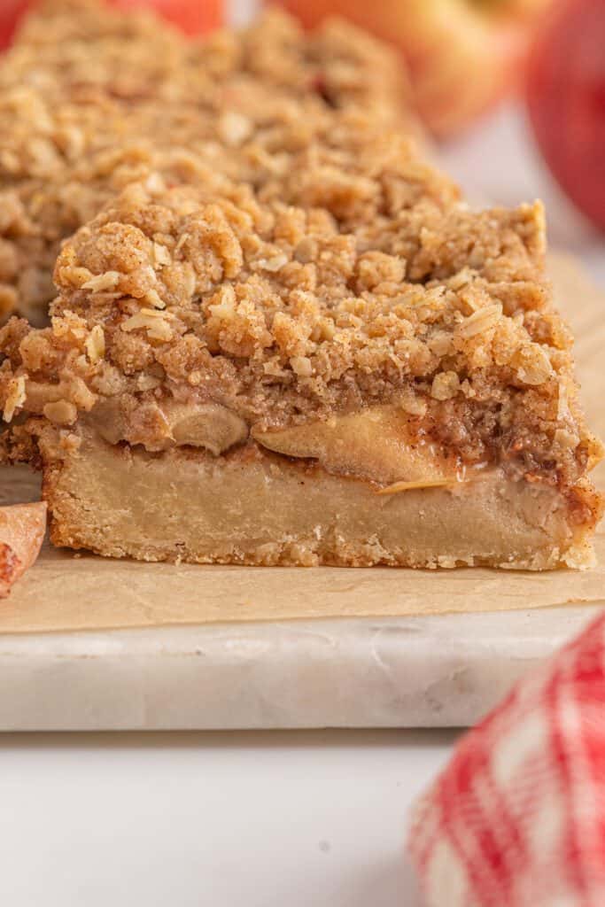 A slice of apple crumble bar on a cutting board with a kitchen towel.