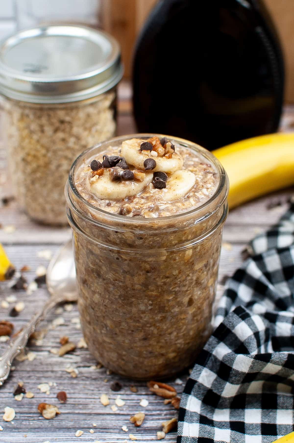 A jar of banana bread overnight oats sitting on a wood countertop with a dish towel.