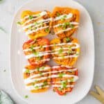Six buffalo chicken pepper halves on a white plate drizzled with ranch dressing.