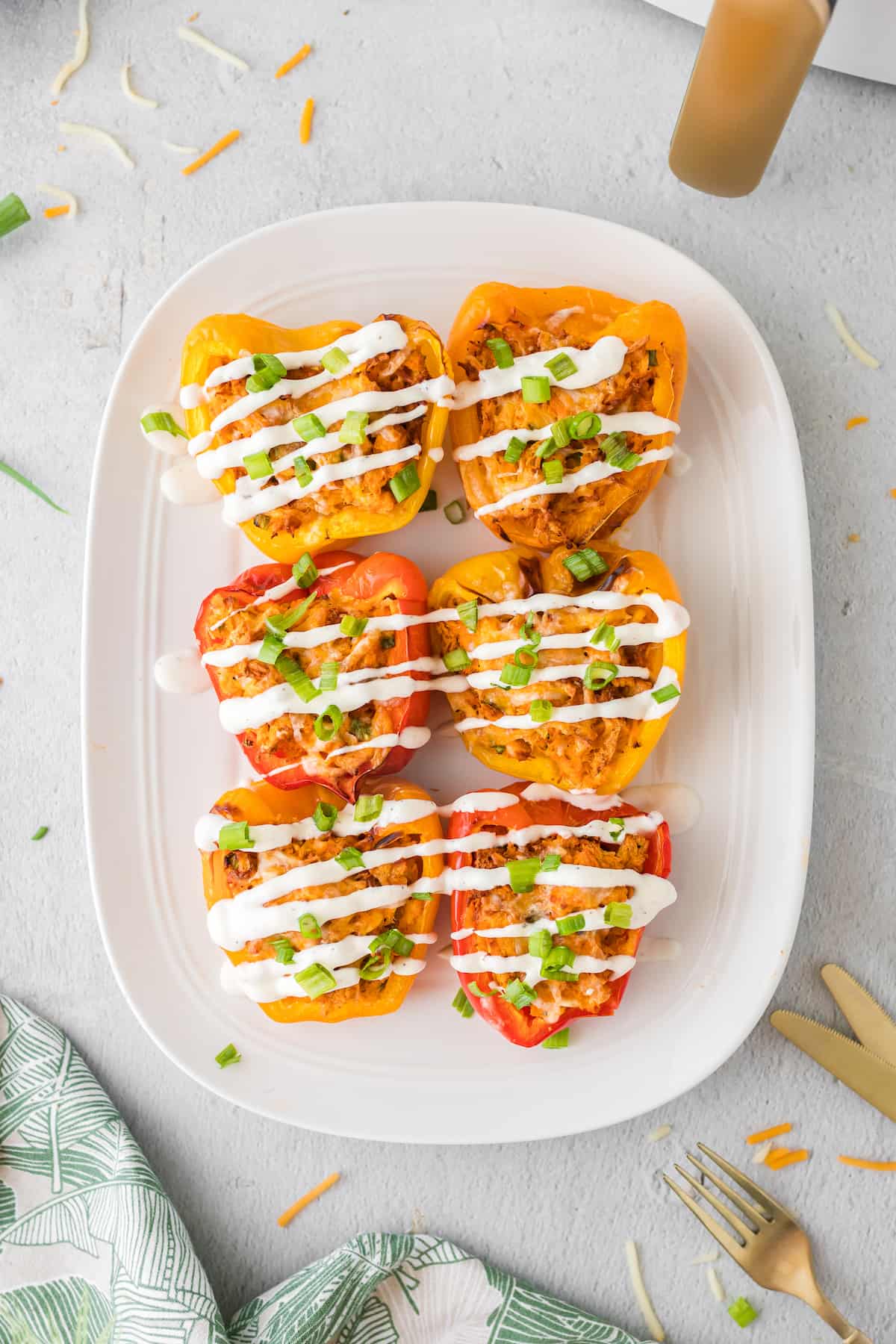 Six buffalo chicken pepper halves on a white plate drizzled with ranch dressing.
