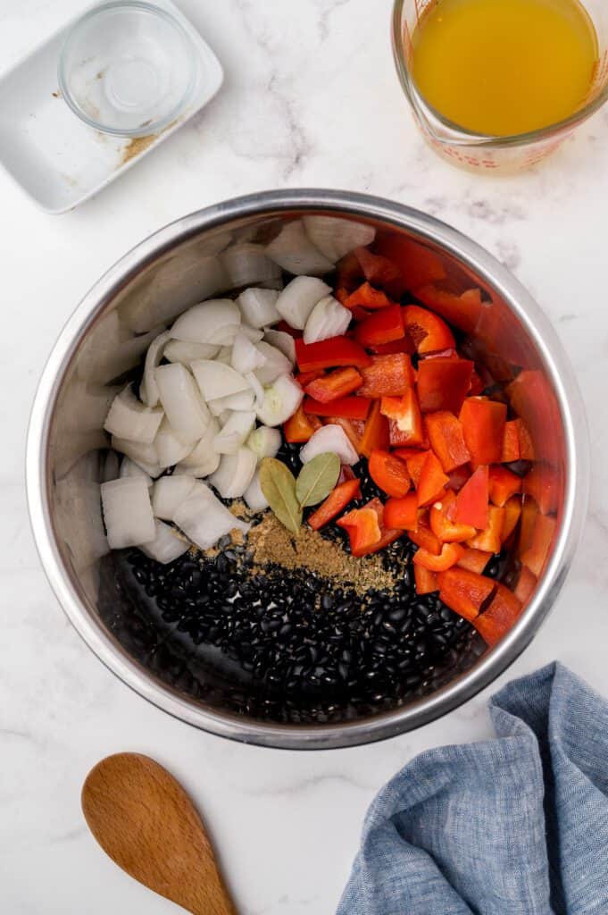 Ingredients in an instant pot including dry black beans, onion, red bell pepper, cumin, oregano.