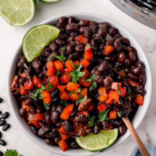 Black beans with bell pepper and lime wedges in a bowl near an Instant Pot.