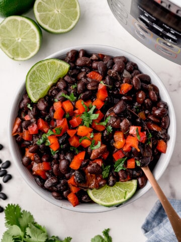 Black beans with bell pepper and lime wedges in a bowl near an Instant Pot.