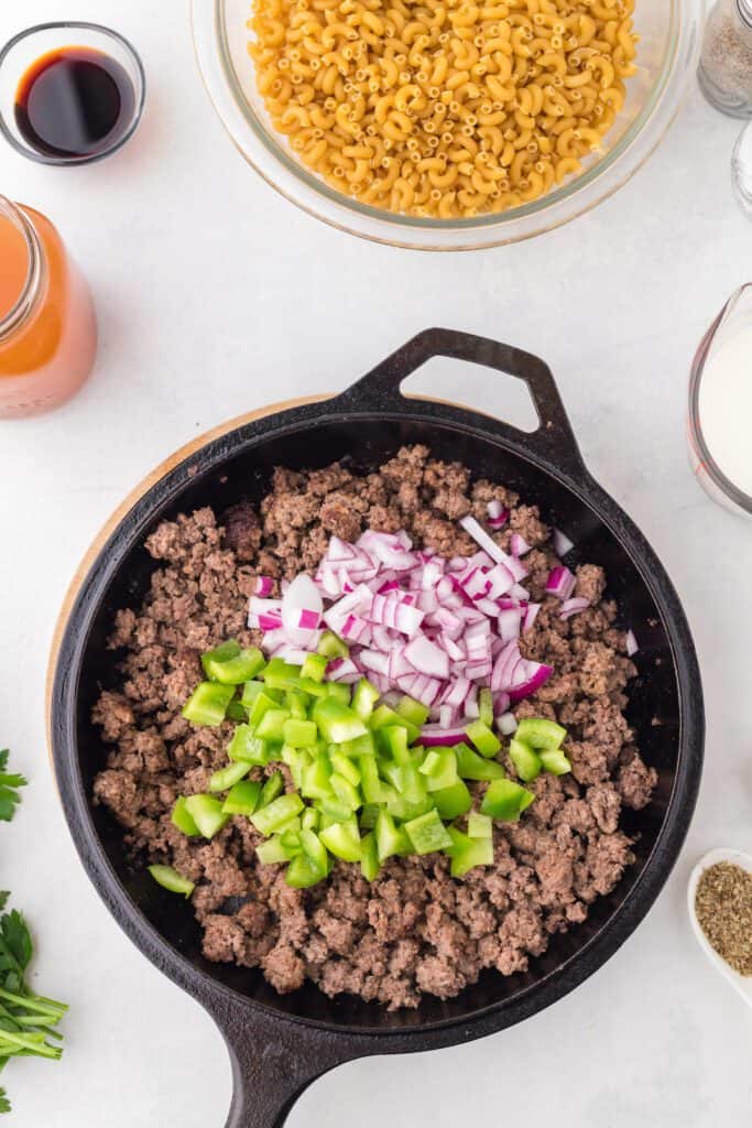 Cooked ground beef, red onion and green bell pepper in a cast iron skillet.