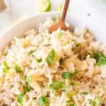 A fork digging into brown rice topped with chopped cilantro leaves.
