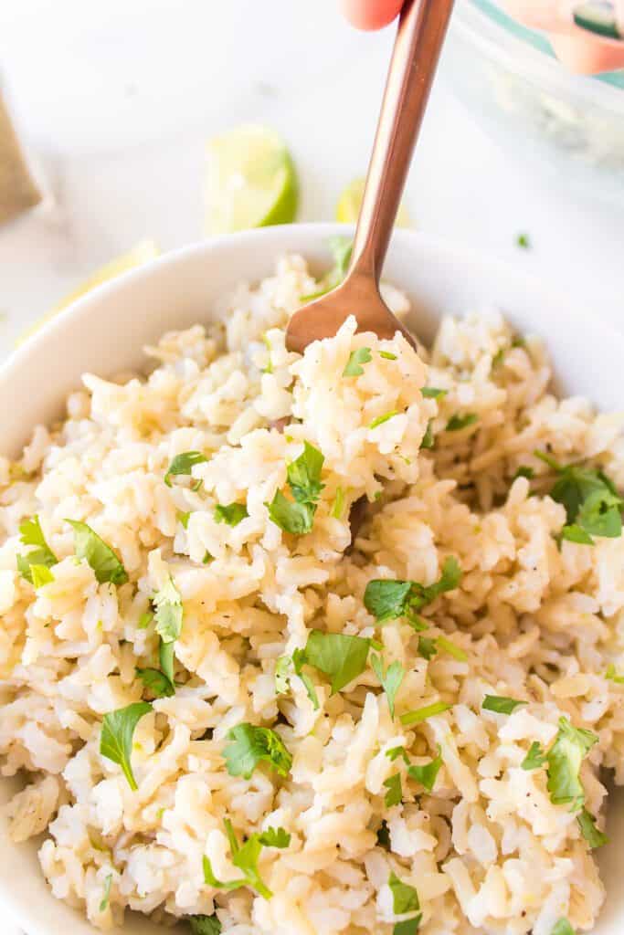 A fork digging into brown rice topped with chopped cilantro leaves.