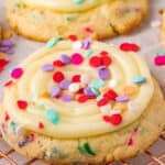 Confetti cookies topped with frosting and sprinkles on a wire rack.