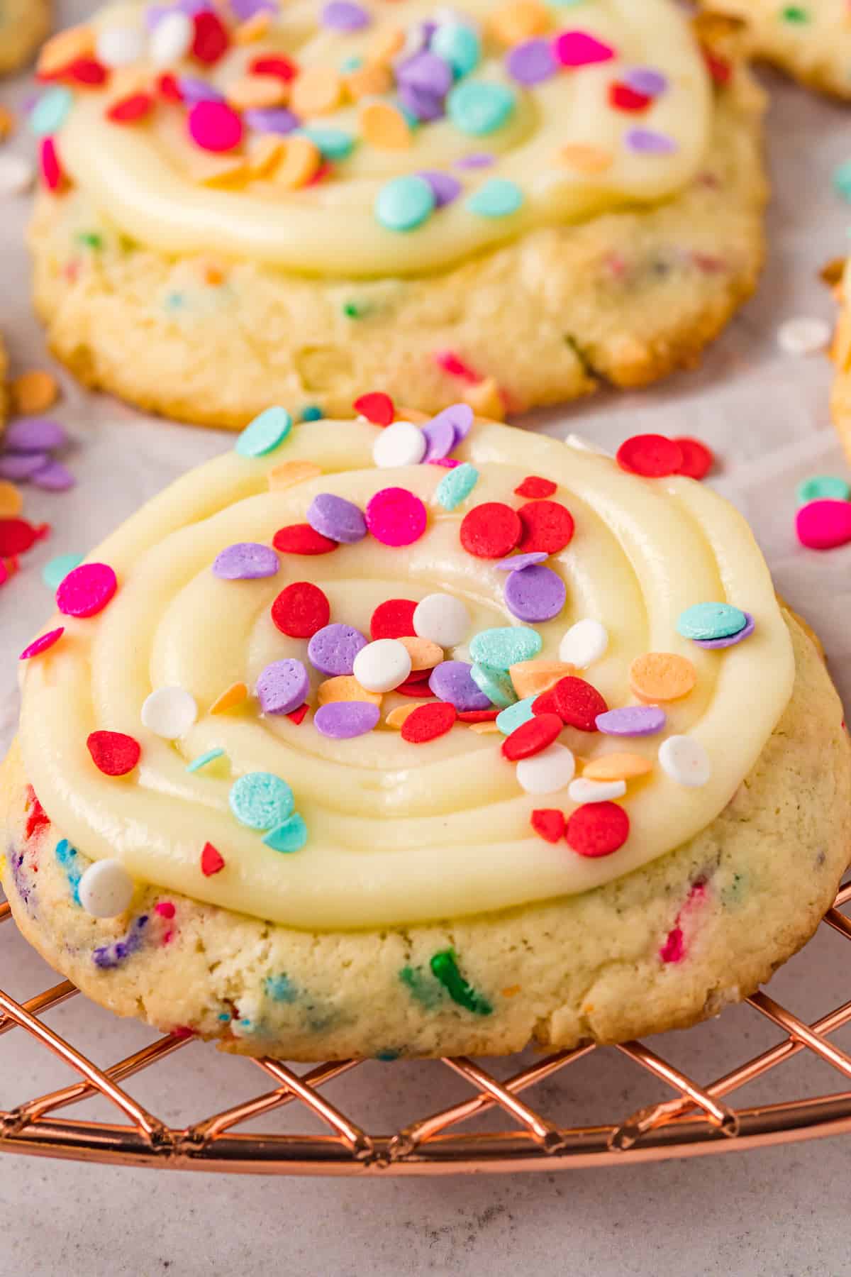 Confetti cookies topped with frosting and sprinkles on a wire rack.