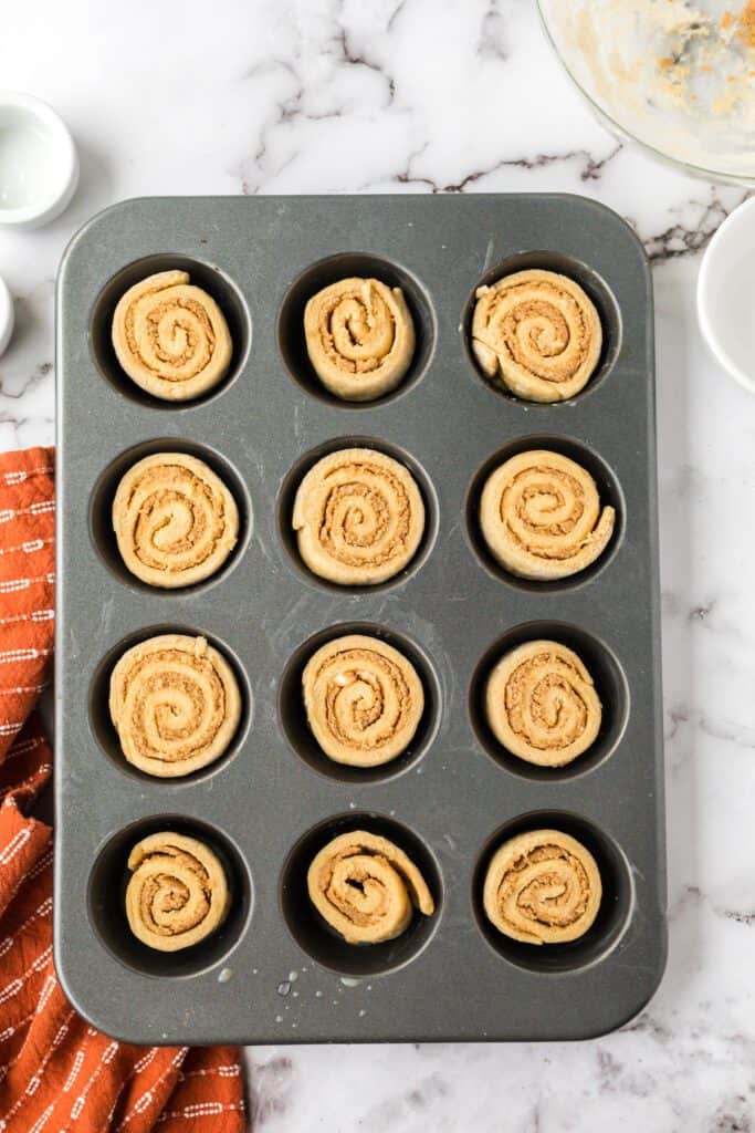 Rolled up cinnamon rolls in a muffin tin.