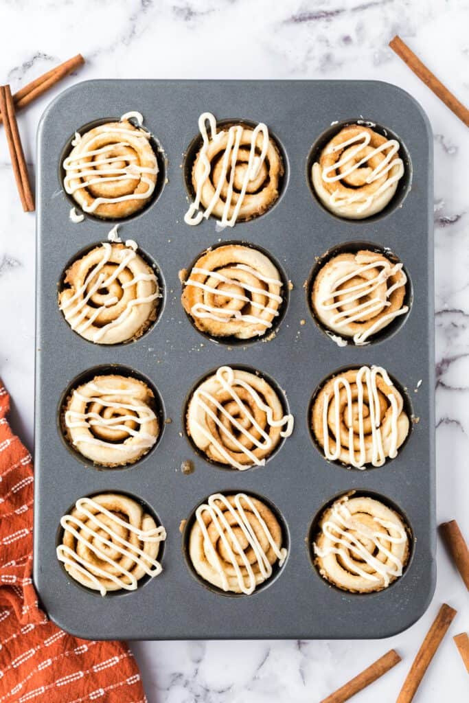Baked cinnamon roll muffins drizzled with icing in a muffin tin.