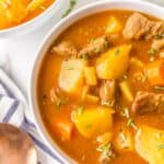 A bowl of beef stew with a spoon and cloth napkin.