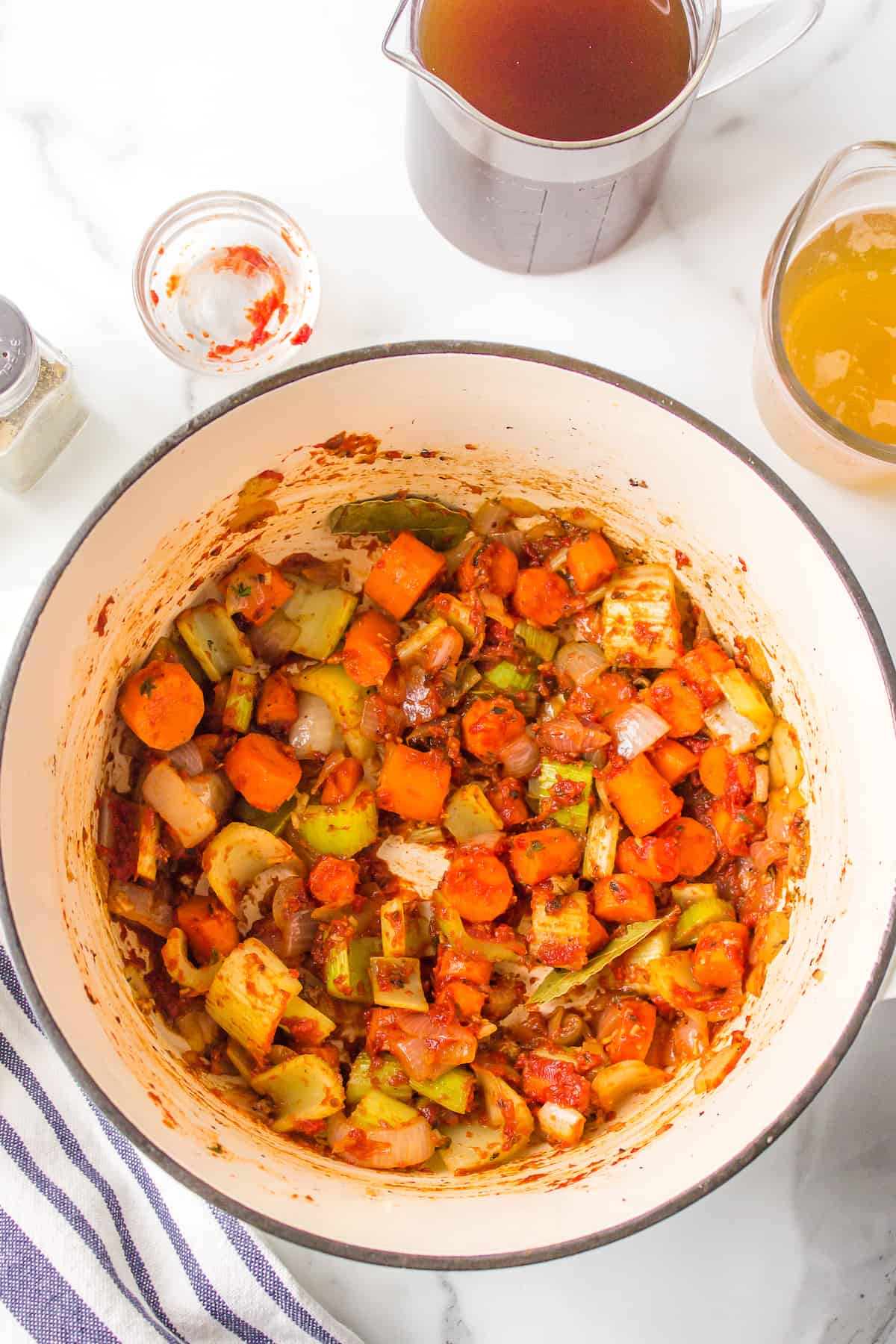 Cooked onion, celery, and carrots with tomato paste in a pot.