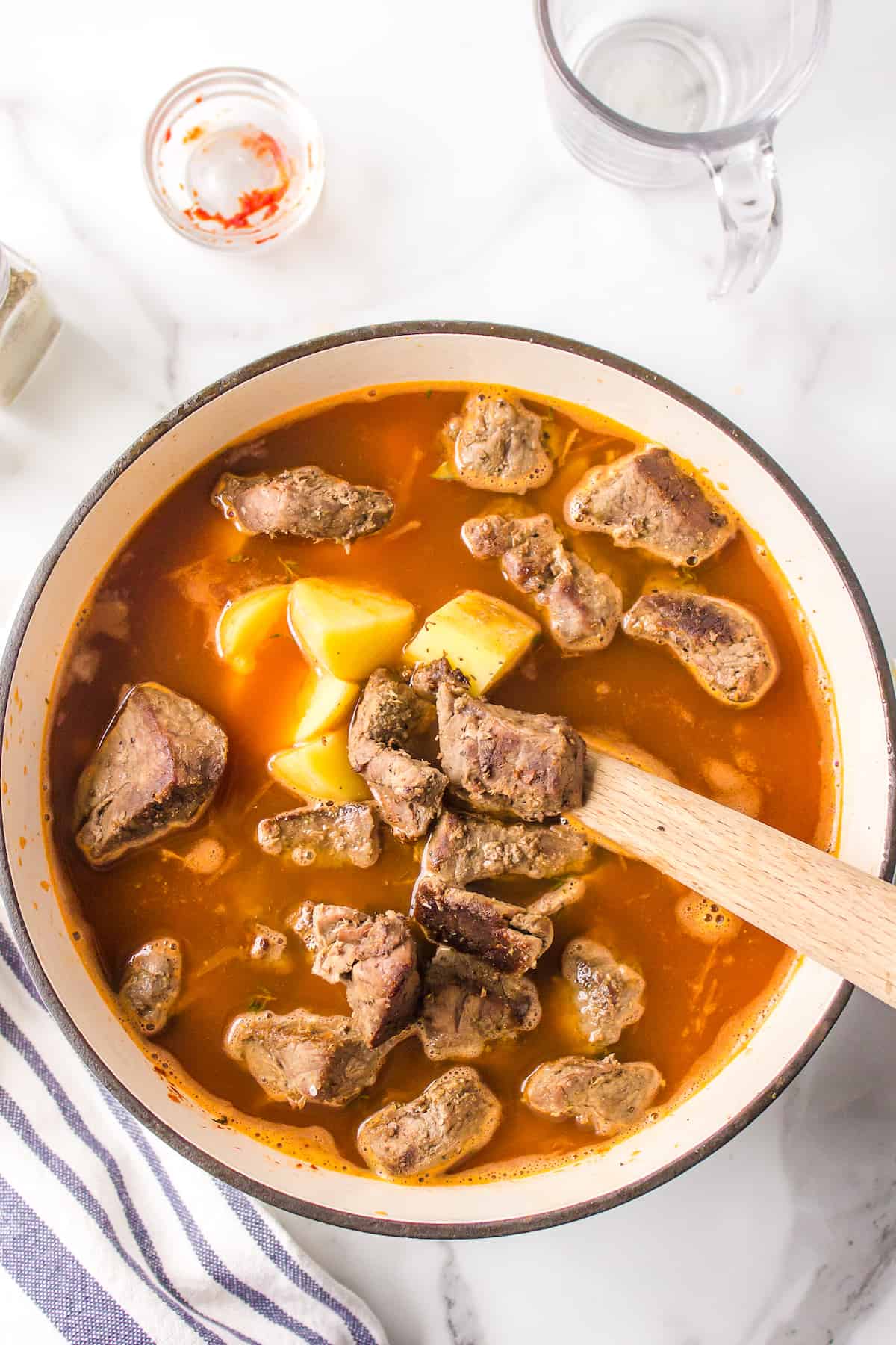 Beef stew meat in a pot with potatoes, vegetables, and beef broth.