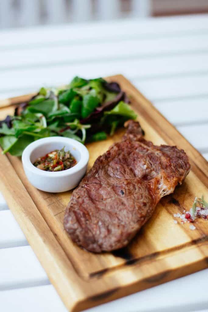 Beef steak on a cutting board with greens.