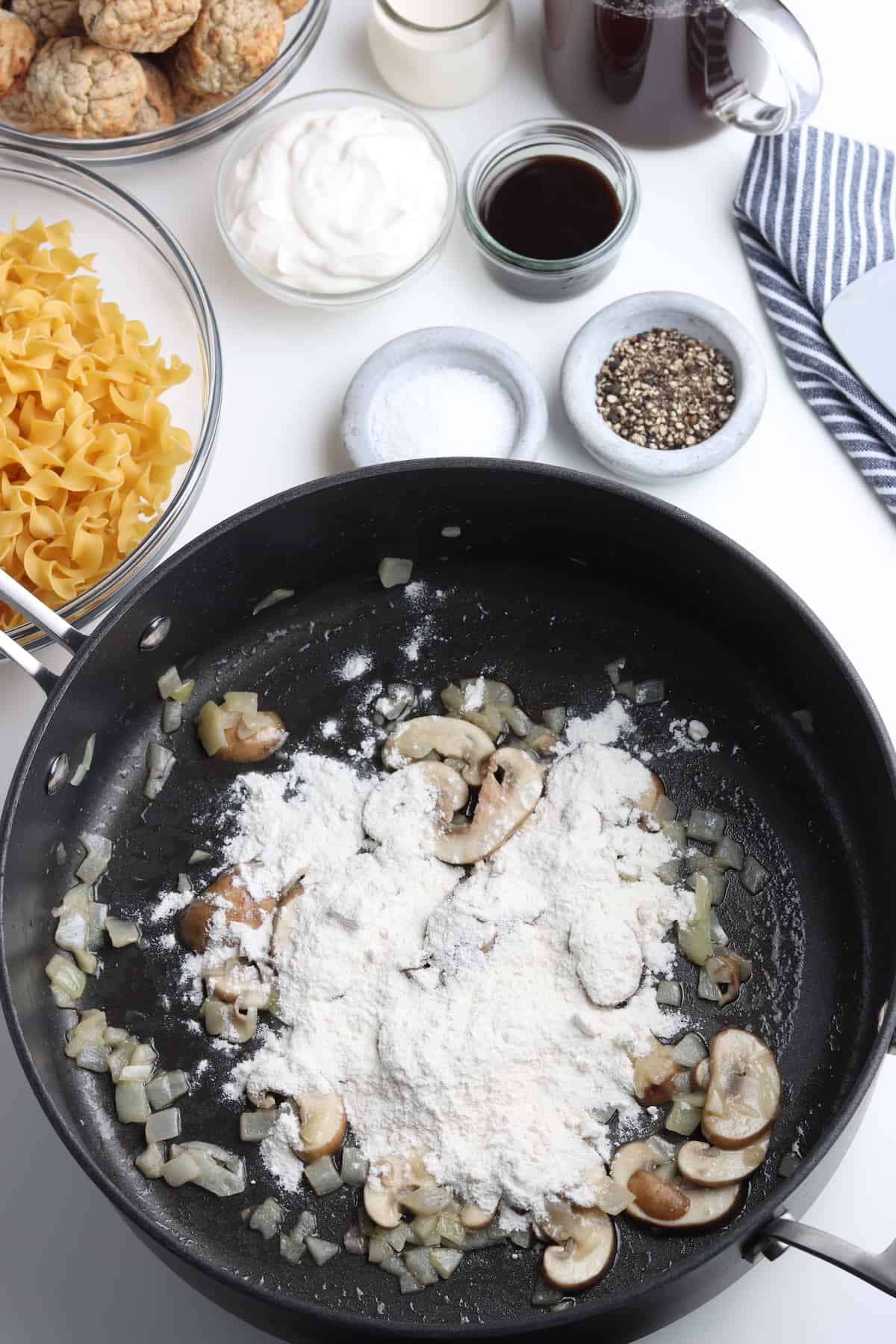 Flour added to mushrooms and onions in a skillet.