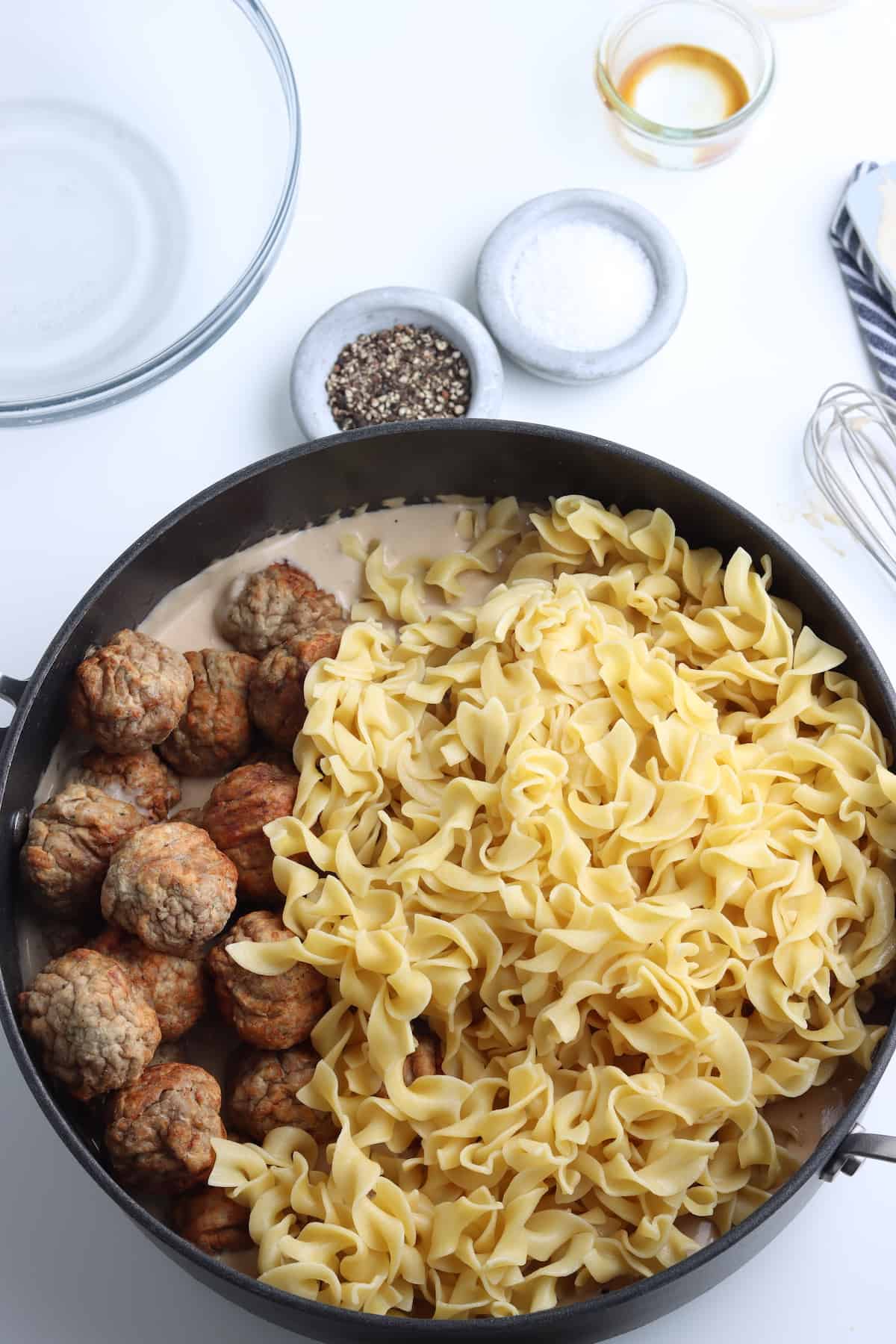 A skillet with meatballs, cooked egg noodles, and a swedish meatball gravy.