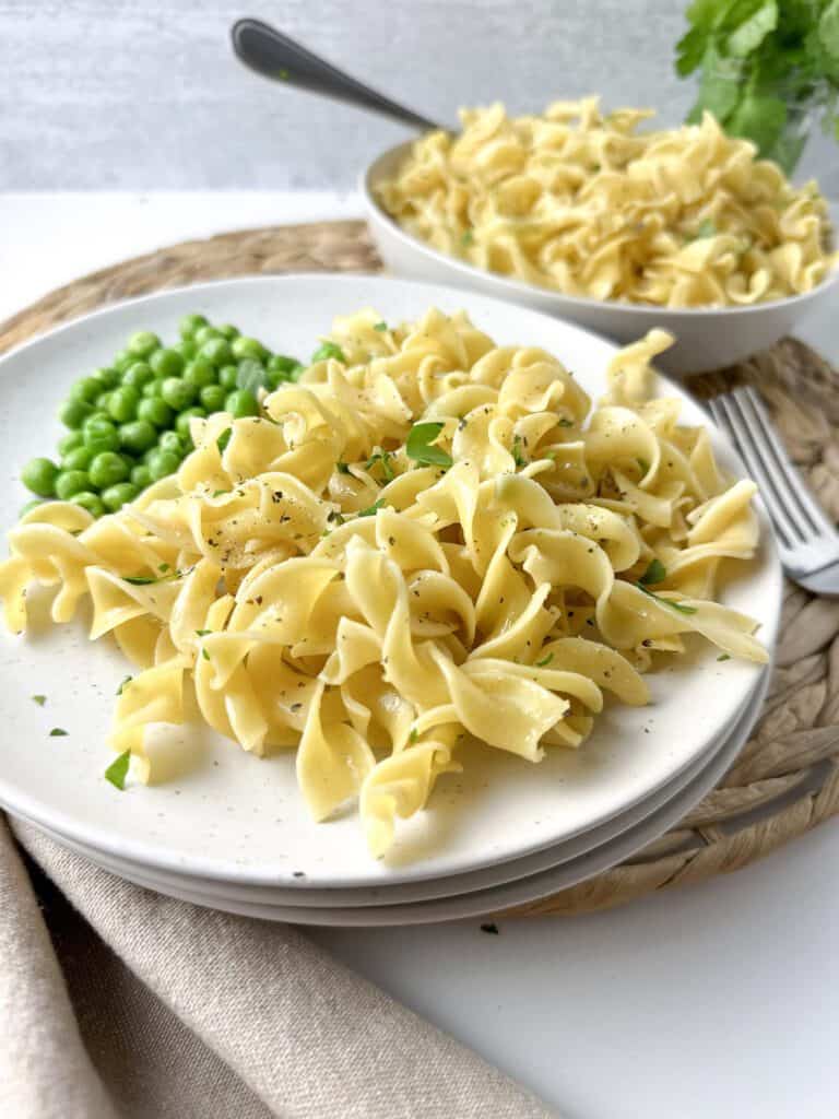 Buttered noodles on a plate with peas.