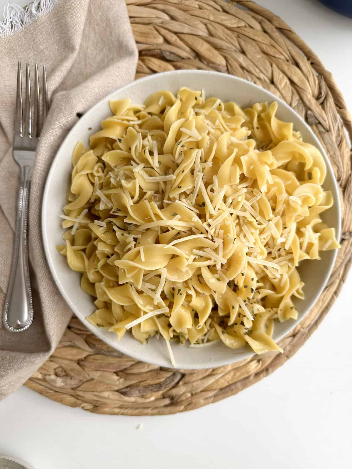Buttered noodles in a bowl with a fork and napkin.