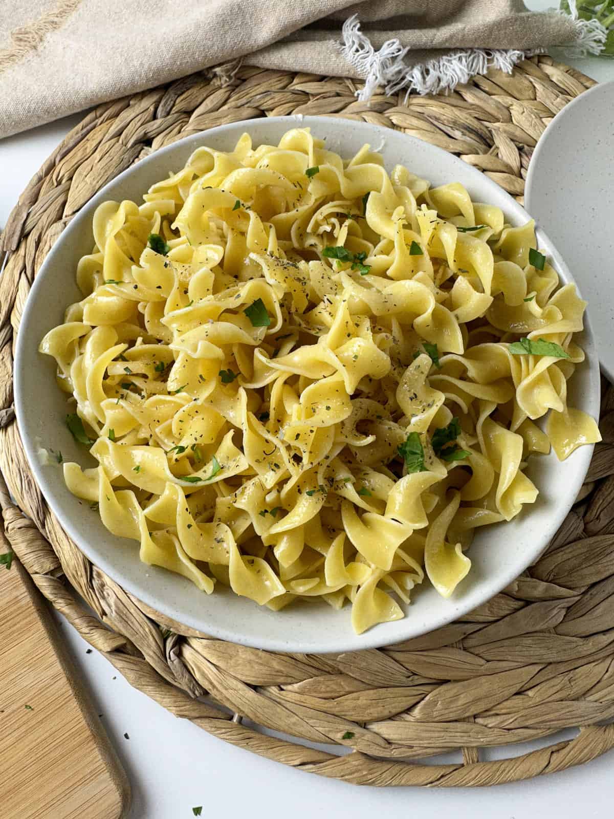 A serving dish of buttered noodles topped with herbs and chopped parsley.