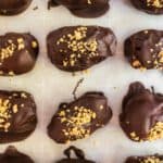 Chocolate covered peanut butter stuffed dates on a baking sheet.