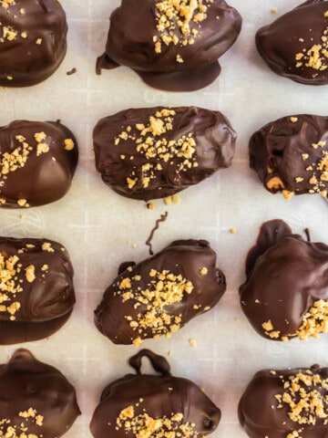 Chocolate covered peanut butter stuffed dates on a baking sheet.