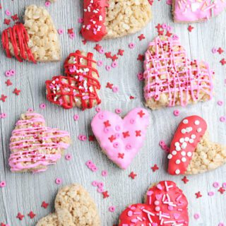 Heart shaped rice krispie treats colored with frosting on a counter.
