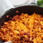 A spoonful of homemade beefaroni by a skillet.