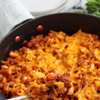 A spoonful of homemade beefaroni by a skillet.