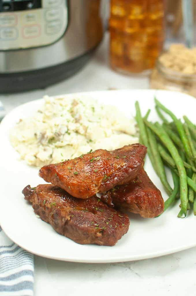 Country style ribs on a plate with mashed potatoes and green beans and an Instant Pot in the background.