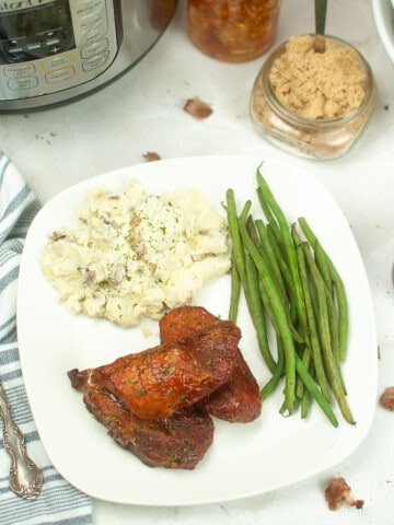 A plate filled with cooked pork ribs, green beans and mashed potatoes.