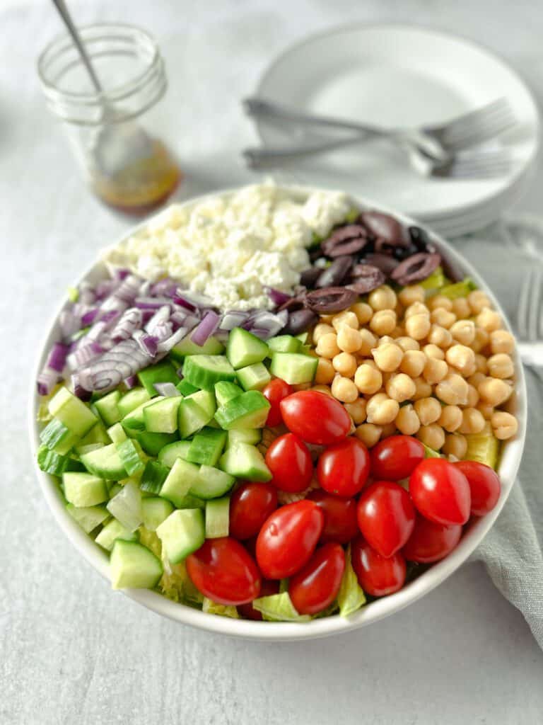 Tomatoes, cucumbers, chickpeas, red onion, kalamato olives and feta cheese in a bowl.