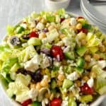 A bowl of chopped romaine lettuce with grape tomatoes, olives, chickpeas and crumbled feta cheese.
