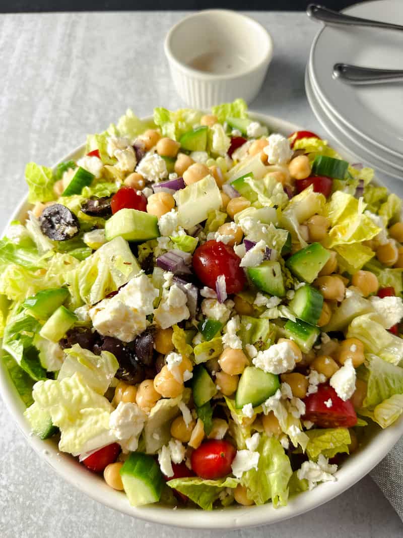 A bowl of chopped romaine lettuce with grape tomatoes, olives, chickpeas and crumbled feta cheese.