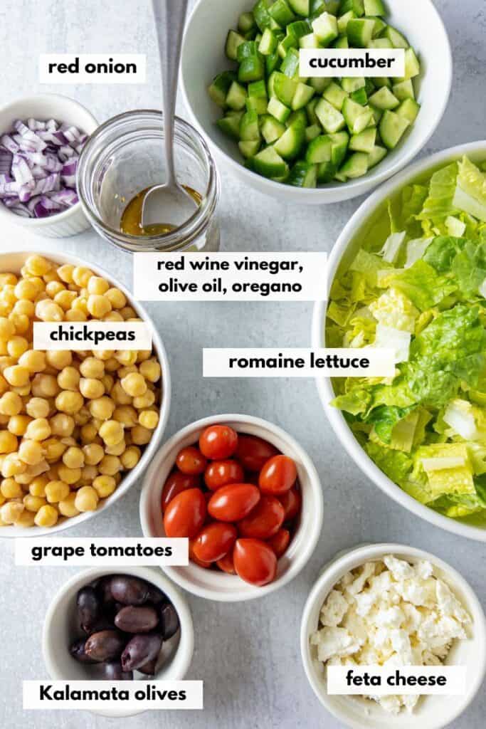 Ingredients in chopped salad including cucumber, red onion, romaine lettuce, chickpeas, tomatoes, red onion, kalamata olives.