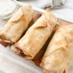A tray of air fried buffalo chicken egg rolls with a small bowl of ranch dressing.