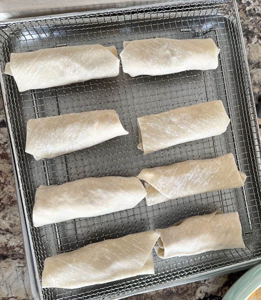 Uncooked buffalo chicken egg rolls on an air fryer tray.
