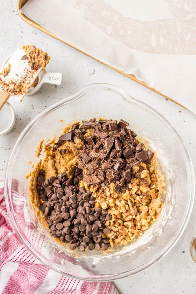 Two types of chocolate and walnuts in a bowl of cookie batter.