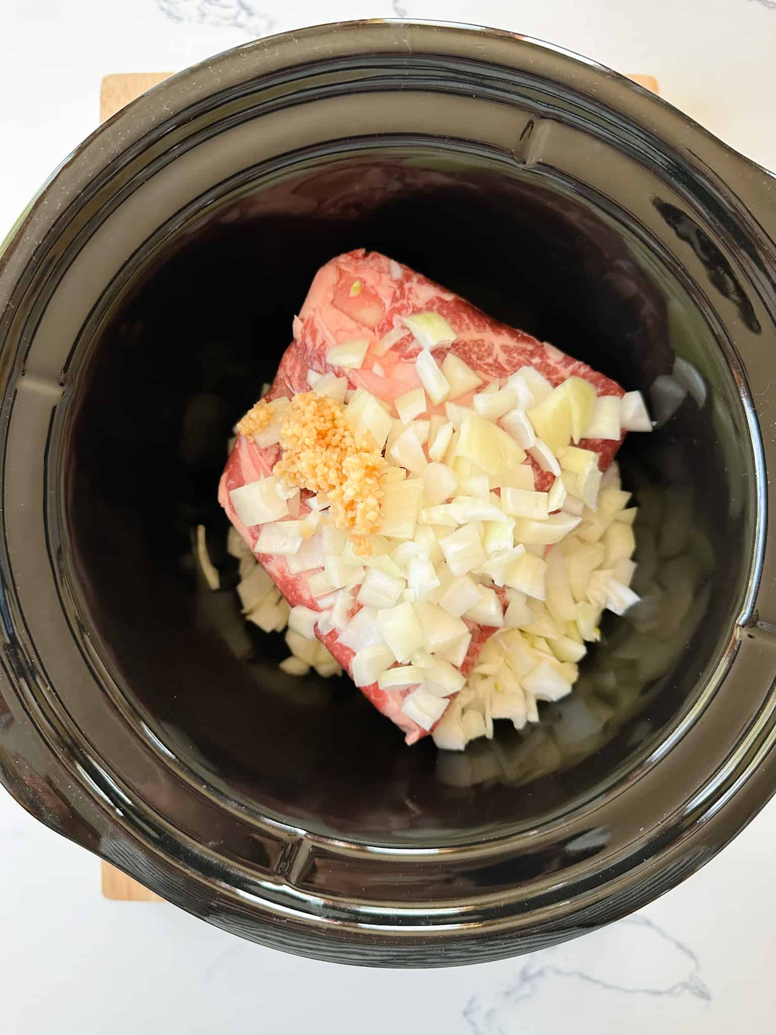 Raw chuck roast placed in slow cooker before cooking Mexican shredded beef.