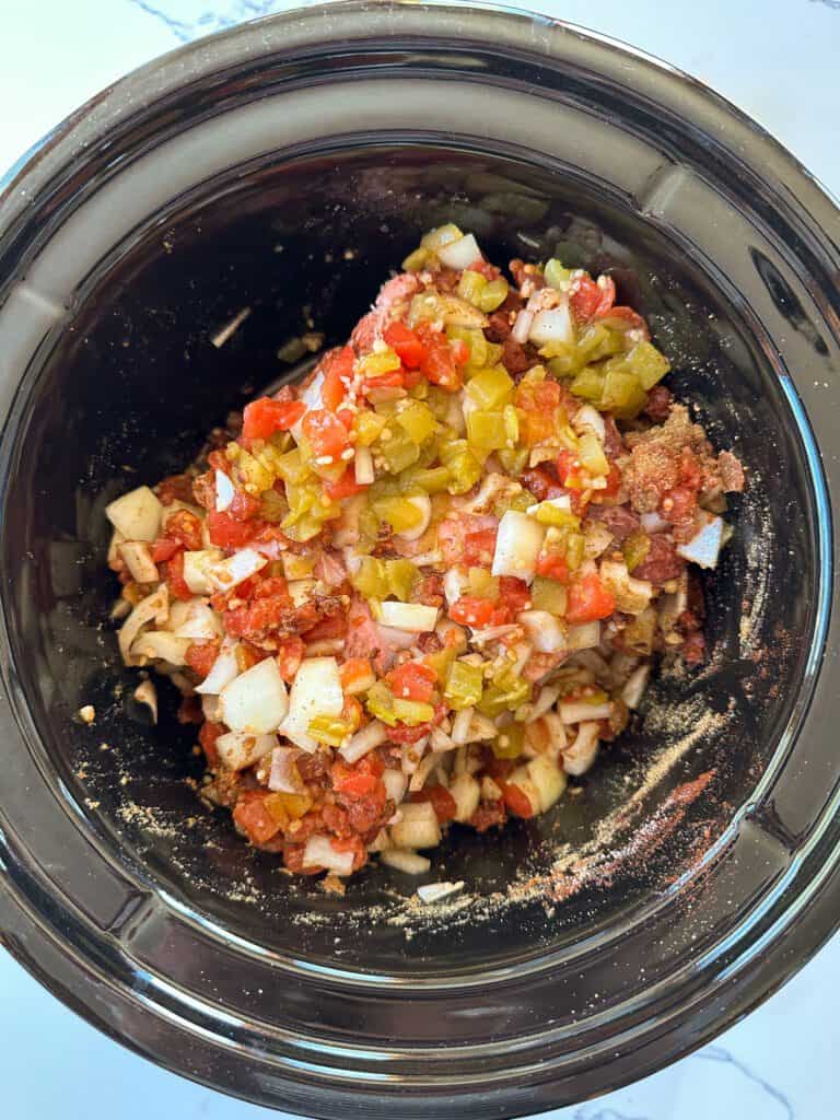 A roast topped with tomatoes, green chilis and dried spices in a slow cooker.