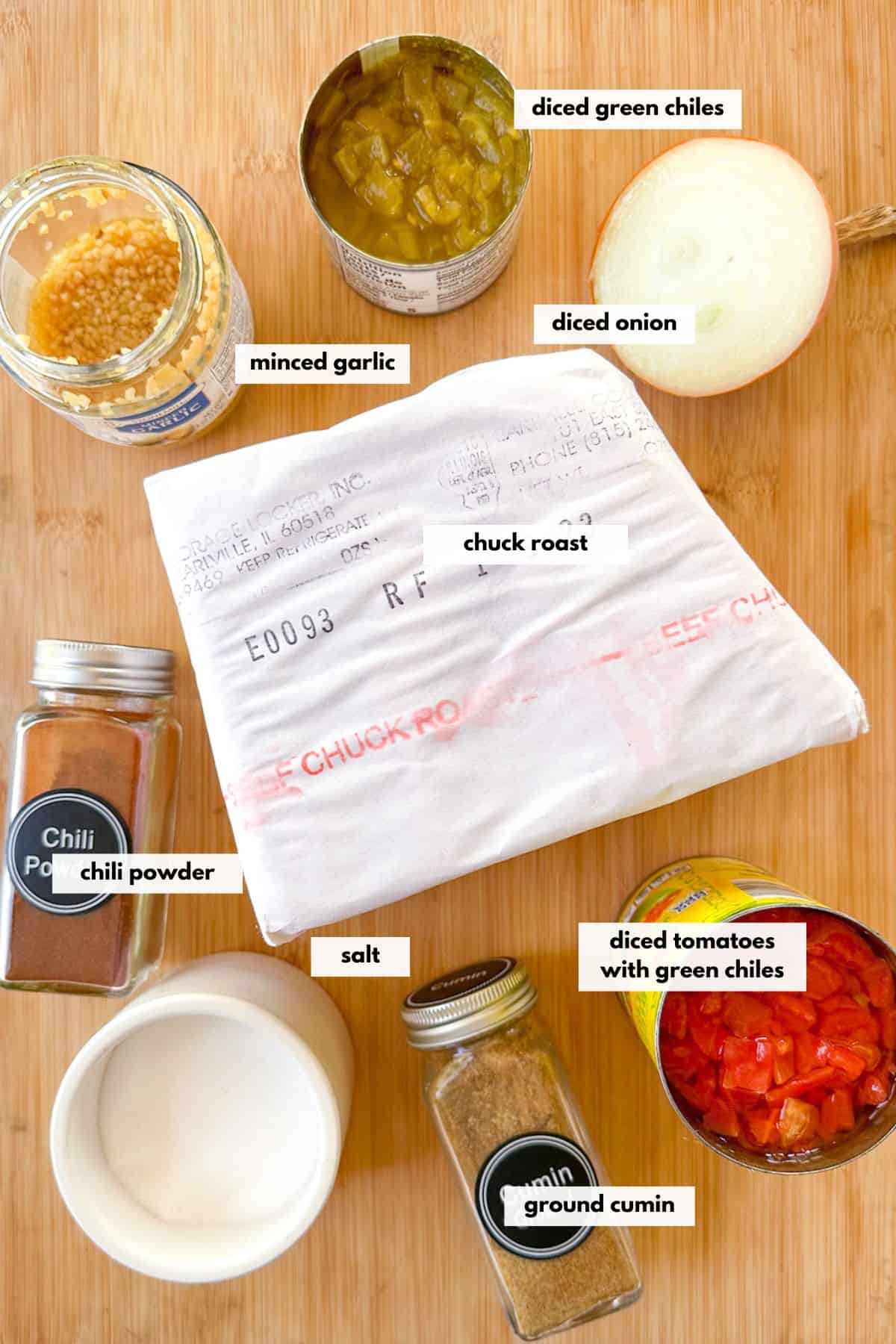 Ingredients to make Mexican shredded beef including chuck roast, minced garlic, green chiles, onion, chili powder, cumin, salt and diced tomatoes.